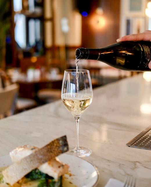 person pouring liquid in clear wine glass